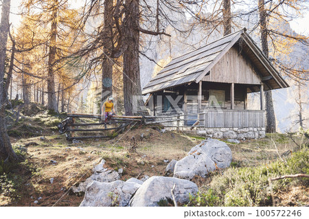 Onle lonley woman hiker sitting on a fence by a wooden house in the forest while on an autumn hike 100572246