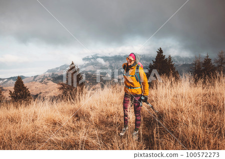 Woman hiking on a cloudy autumn day in colorful outwear, yellow jacket and pink leggings  100572273