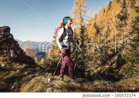 Cheerful caucasian woman hiking on a sunny autumn day, soaking in the mountain sun  100572274