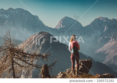 Back view of female mountaineer enjoying the view of autumn mountains on a sunny cold day 100572292