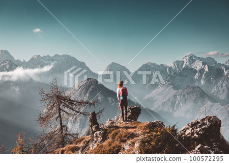 Scenic mountain view and one lonely woman hiker standing at a view point looking at the Alps 100572295