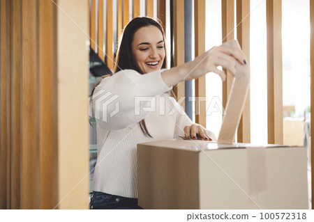 Smiling woman opening a delivery package with excitement Smiling woman opening a delivery package with excitement 100572318