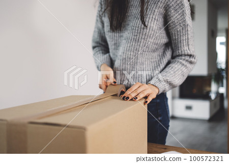 Unrecognizable woman taping a cardboard box, sending Christmas presents to family  100572321