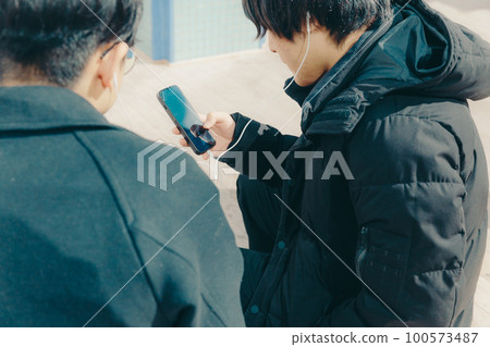 A picture of a male college student listening to music with earphones in the park A picture of a male college student listening to music with earphones in the park 100573487
