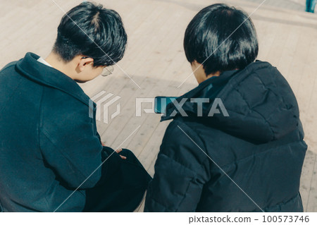 A picture of a male college student touching a smartphone in the park 100573746