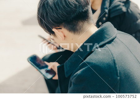 A picture of a male college student touching a smartphone in the park A picture of a male college student touching a smartphone in the park 100573752