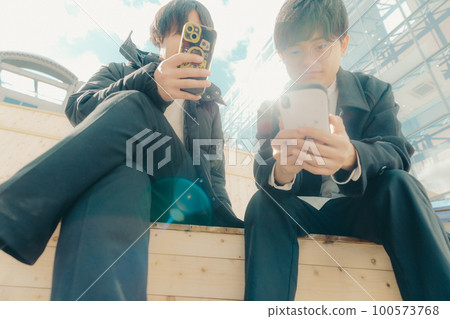 A picture of a male college student touching a smartphone in the park 100573768