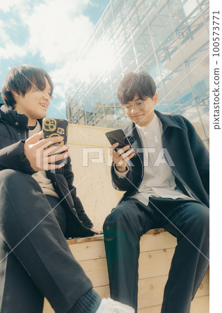 A picture of a male college student touching a smartphone in the park 100573771