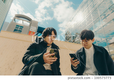 A picture of a male college student touching a smartphone in the park A picture of a male college student touching a smartphone in the park 100573773