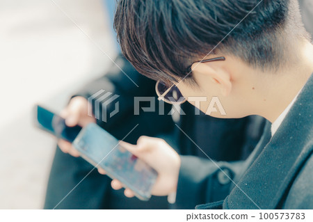 一張男大學生在公園裡摸智能手機的照片 100573783