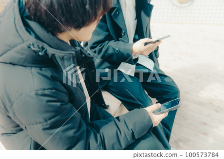 A picture of a male college student touching a smartphone in the park 100573784
