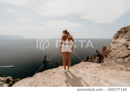 Woman travel sea. Young Happy woman posing on a beach over the sea on background of volcanic rocks, like in Iceland, sharing travel adventure journey 100577146