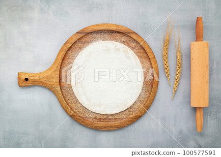 Homemade pizza dough in wooden pizza platter with wheat ears set up on grey concrete background flat lay and copy space 100577591