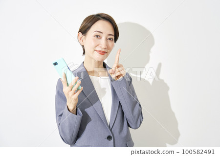 拿著智能手機並且指向正確的白色背景的女商人 拿著智能手機並且指向正確的白色背景的女商人 100582491