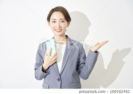 Business woman holding a smartphone and pointing to the right with her palm White background Business woman holding a smartphone and pointing to the right with her palm White background 100582492