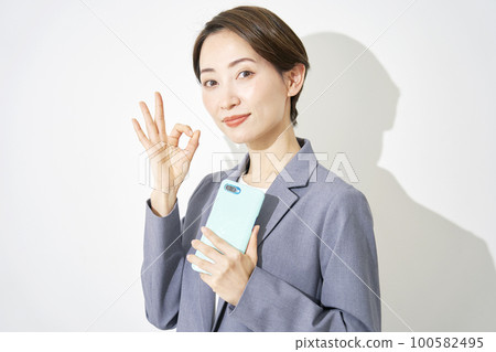 Business woman holding a smartphone and signing OK white background Business woman holding a smartphone and signing OK white background 100582495
