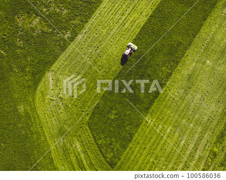 Drone photo of tractor mowing a green grass field in the countryside on a sunny day Drone photo of tractor mowing a green grass field in the countryside on a sunny day 100586036
