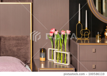 Fresh blooming red tulips in stylish vases made of glass transparent test tubes on the bedside table decorate the headboard. Fresh blooming red tulips in stylish vases made of glass transparent test tubes on the bedside table decorate the headboard. 100586110