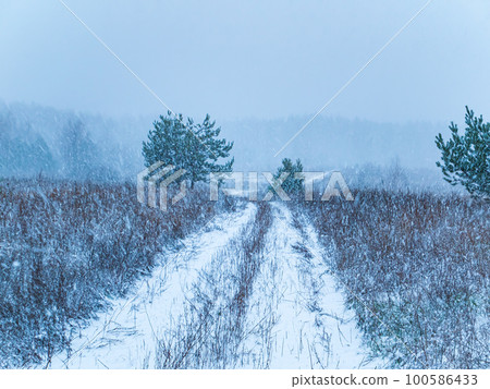 The dirt road is covered with snow of a winter blizzard. 100586433