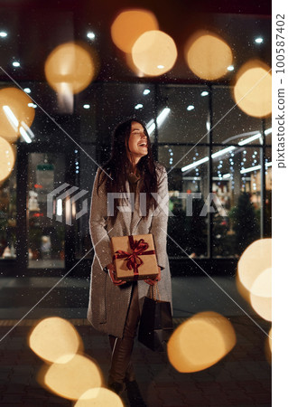 With present in hands. Cheerful woman is outdoors at Christmas holidays time. Conception of new year With present in hands. Cheerful woman is outdoors at Christmas holidays time. Conception of new year 100587402