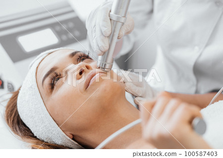Electroporation without injection mesotherapy. Woman cosmetologist performs cosmetic procedure  100587403