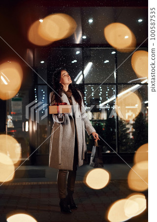 Holds gift box in hands. Cheerful woman is outdoors at Christmas holidays time. Conception of new year Holds gift box in hands. Cheerful woman is outdoors at Christmas holidays time. Conception of new year 100587535
