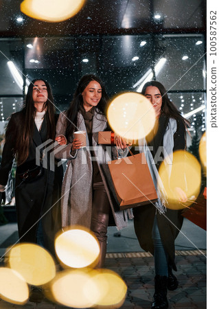 Cups of drink in hands. Three cheerful women spends Christmas holidays together outdoors. Conception of new year 100587562