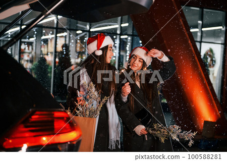 Standing near car's back trunk opened. Happy sisters twins spends Christmas holidays together outdoors. Conception of new year Standing near car's back trunk opened. Happy sisters twins spends Christmas holidays together outdoors. Conception of new year 100588281