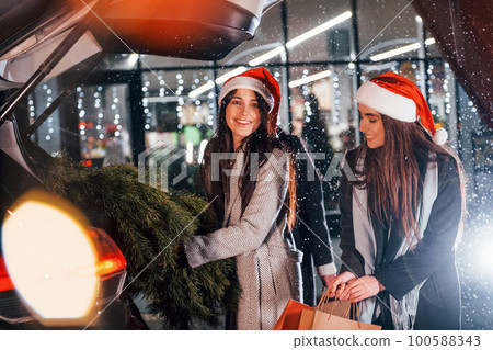 Holds fir. Three cheerful women spends Christmas holidays together outdoors. Conception of new year 100588343