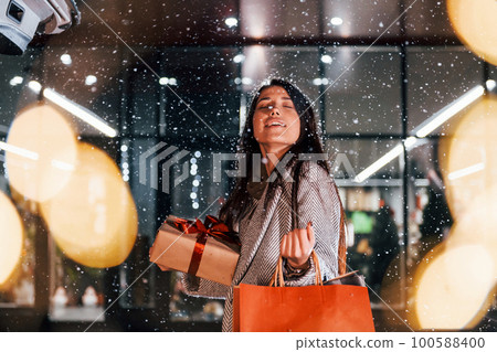 Near the car with gift box. Cheerful woman is outdoors at Christmas holidays time. Conception of new year Near the car with gift box. Cheerful woman is outdoors at Christmas holidays time. Conception of new year 100588400