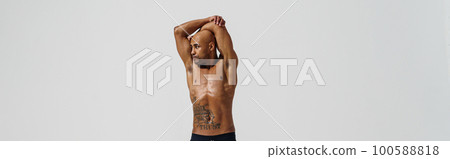 Attractive sportsman with naked torso is warming up on white studio background before workout Attractive sportsman with naked torso is warming up on white studio background before workout 100588818
