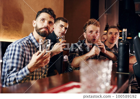 Expressive people watching soccer. Group of people together indoors in the pub have fun at weekend time Expressive people watching soccer. Group of people together indoors in the pub have fun at weekend time 100589192