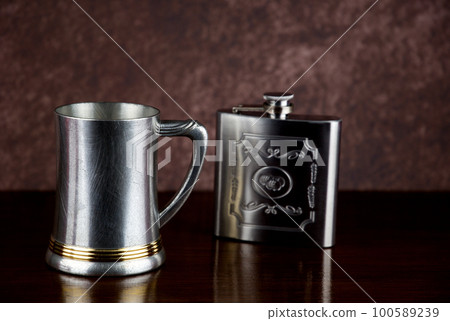Old Pewter Tankard and Steel Hip Flask on a Wooden Shelf Old Pewter Tankard and Steel Hip Flask on a Wooden Shelf 100589239