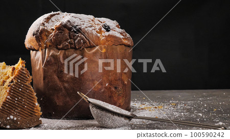 Panettone biscuit with dried fruits on a black background and sprinkled with powdered sugar 100590242
