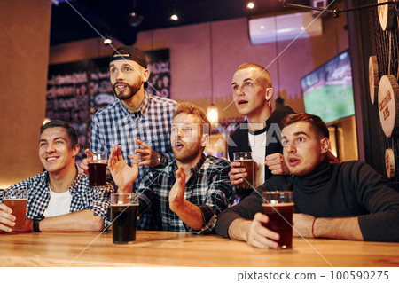 Football fans watching TV. Group of people together indoors in the pub have fun at weekend time Football fans watching TV. Group of people together indoors in the pub have fun at weekend time 100590275