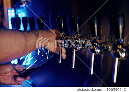 Man pour alcohol in the glass. Close up view of beer taps in a pub. Artifical blue lighting 100590342