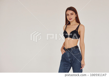 Young woman in jeans and bra indoors. White background Young woman in jeans and bra indoors. White background 100591147