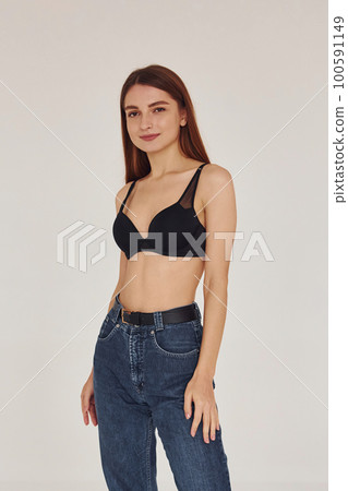 Young woman in jeans and bra indoors. White background Young woman in jeans and bra indoors. White background 100591149