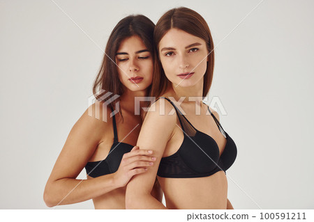 Two young women in lingerie together indoors. White background 100591211