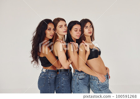 Leaning on each other. Four young women in lingerie together indoors. White background 100591268