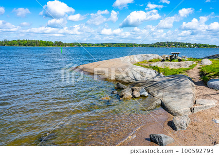 Small beach with flat stones, a bench, and an amazing view of other islands on a sunny summer day. Island of Vaxholm, Stockholm Archipelago, Sweden 100592793