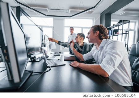 Team of stockbrokers works in modern office with many display screens 100593104