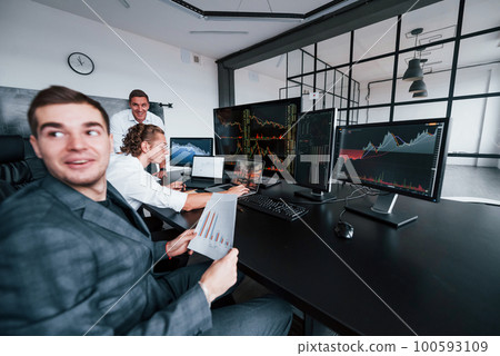 Holds document in hands. Team of stockbrokers works in modern office with many display screens Holds document in hands. Team of stockbrokers works in modern office with many display screens 100593109