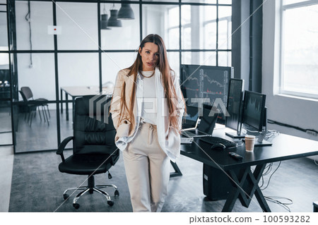 Poses for the camera. Young female stock brocker is indoors in the office. Many of displays Poses for the camera. Young female stock brocker is indoors in the office. Many of displays 100593282