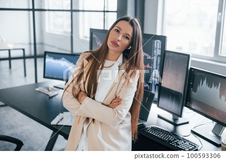 Poses for the camera. Young female stock brocker is indoors in the office. Many of displays Poses for the camera. Young female stock brocker is indoors in the office. Many of displays 100593306