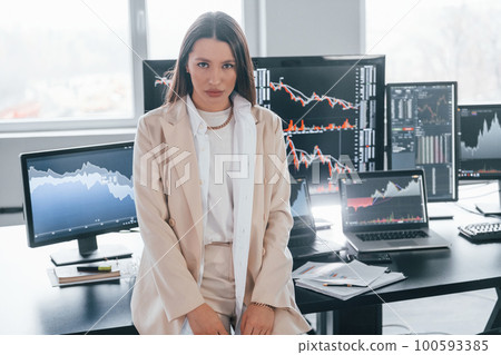 Poses for the camera. Young female stock brocker is indoors in the office. Many of displays Poses for the camera. Young female stock brocker is indoors in the office. Many of displays 100593385