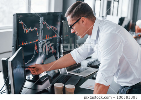 In formal clothes. Young male stock brocker works indoors in the office. Many of displays 100593393