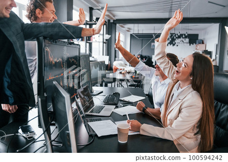 Giving high five. Team of stockbrokers works in modern office with many display screens Giving high five. Team of stockbrokers works in modern office with many display screens 100594242