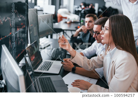 Analysing information. Team of stockbrokers works in modern office with many display screens 100594257