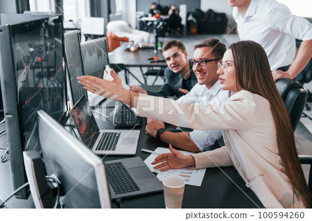 Analysing information. Team of stockbrokers works in modern office with many display screens Analysing information. Team of stockbrokers works in modern office with many display screens 100594260